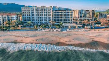 A beachfront hotel with multiple buildings, a sandy beach, and a clear view of the ocean.