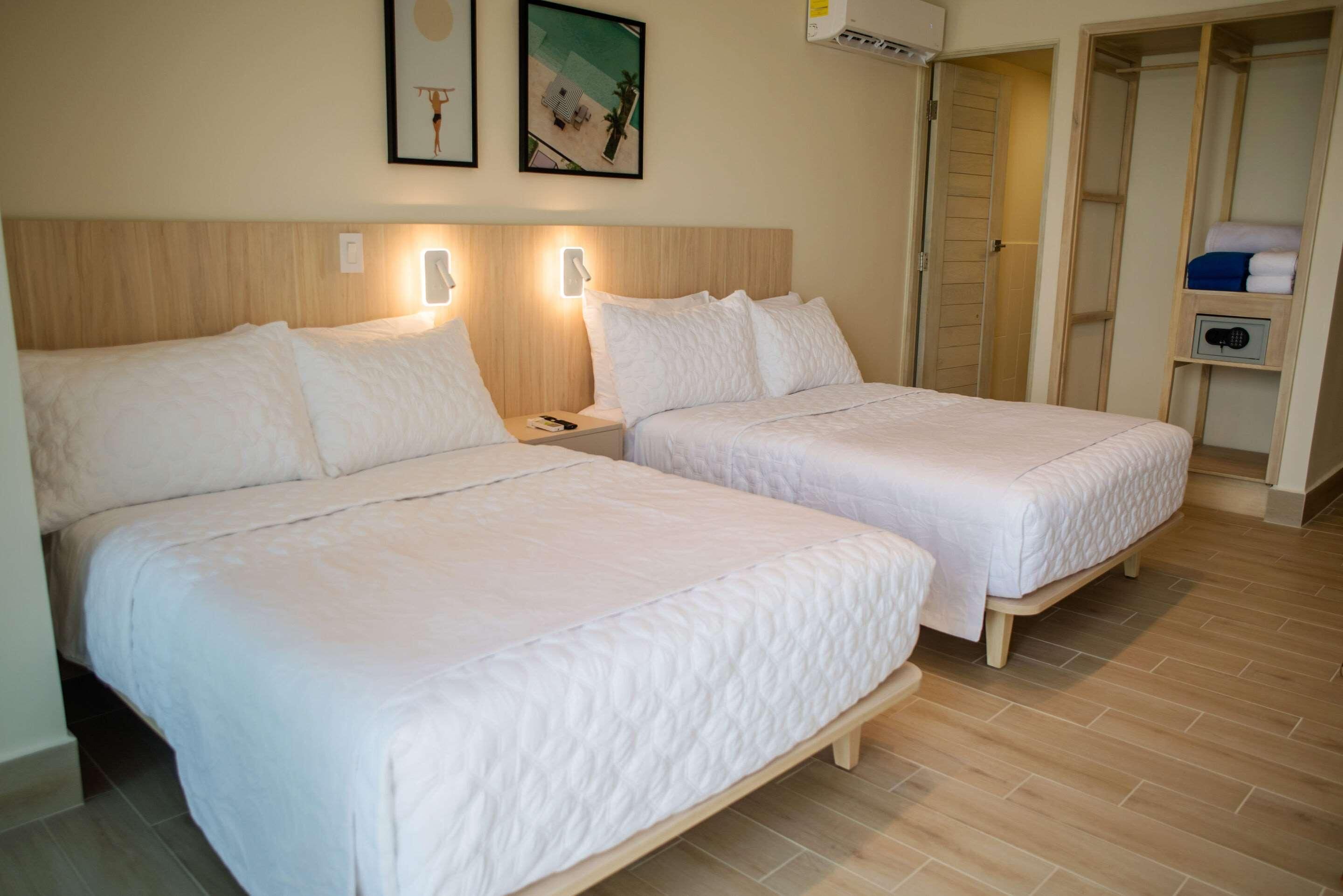 A hotel room with two beds, a wooden headboard, bedside lamps, a small table, and a wardrobe with a lock.