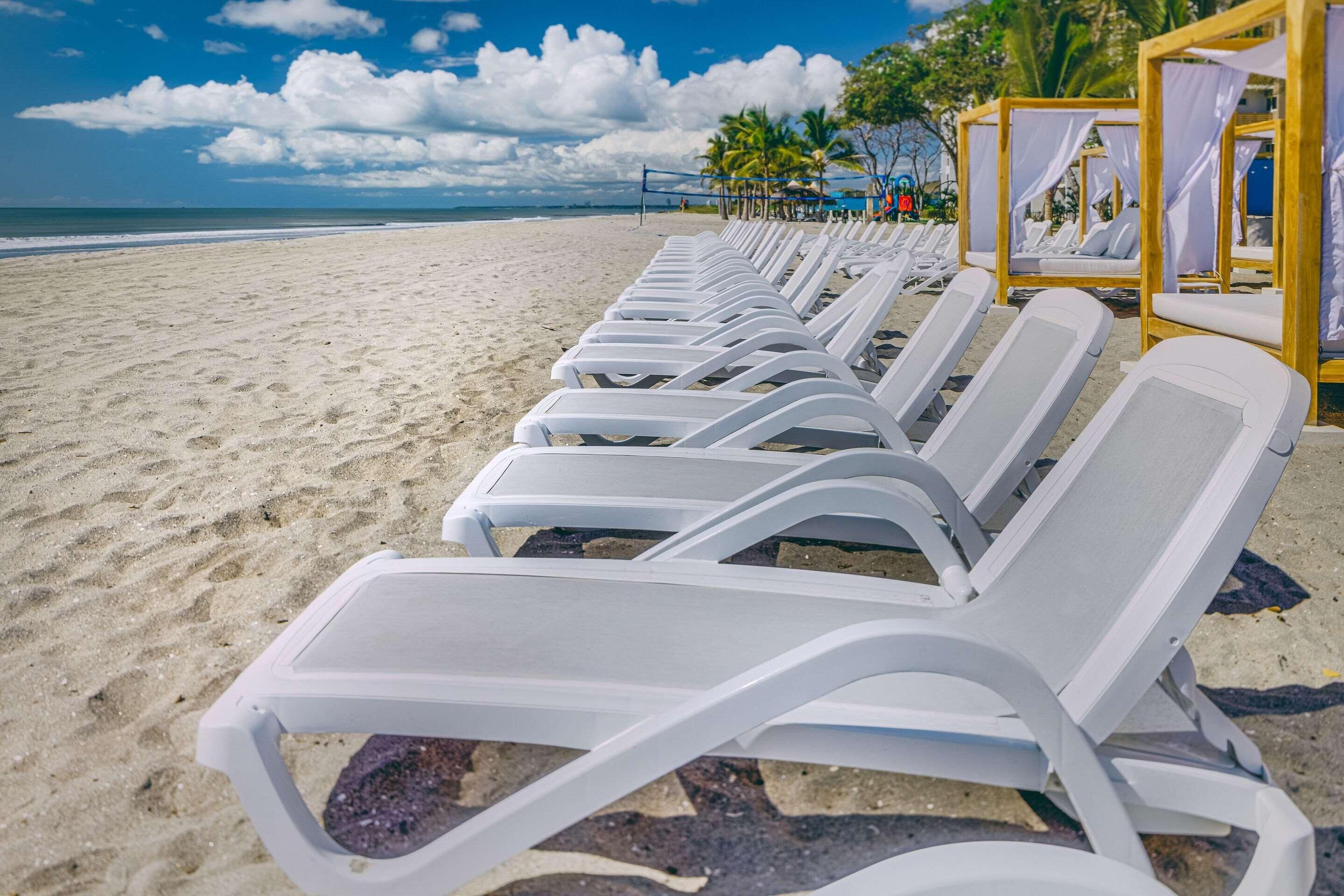 A beach with rows of white sun loungers aligned parallel to the shoreline.