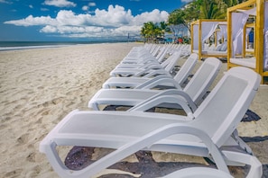 A beach with rows of white sun loungers aligned parallel to the shoreline.
