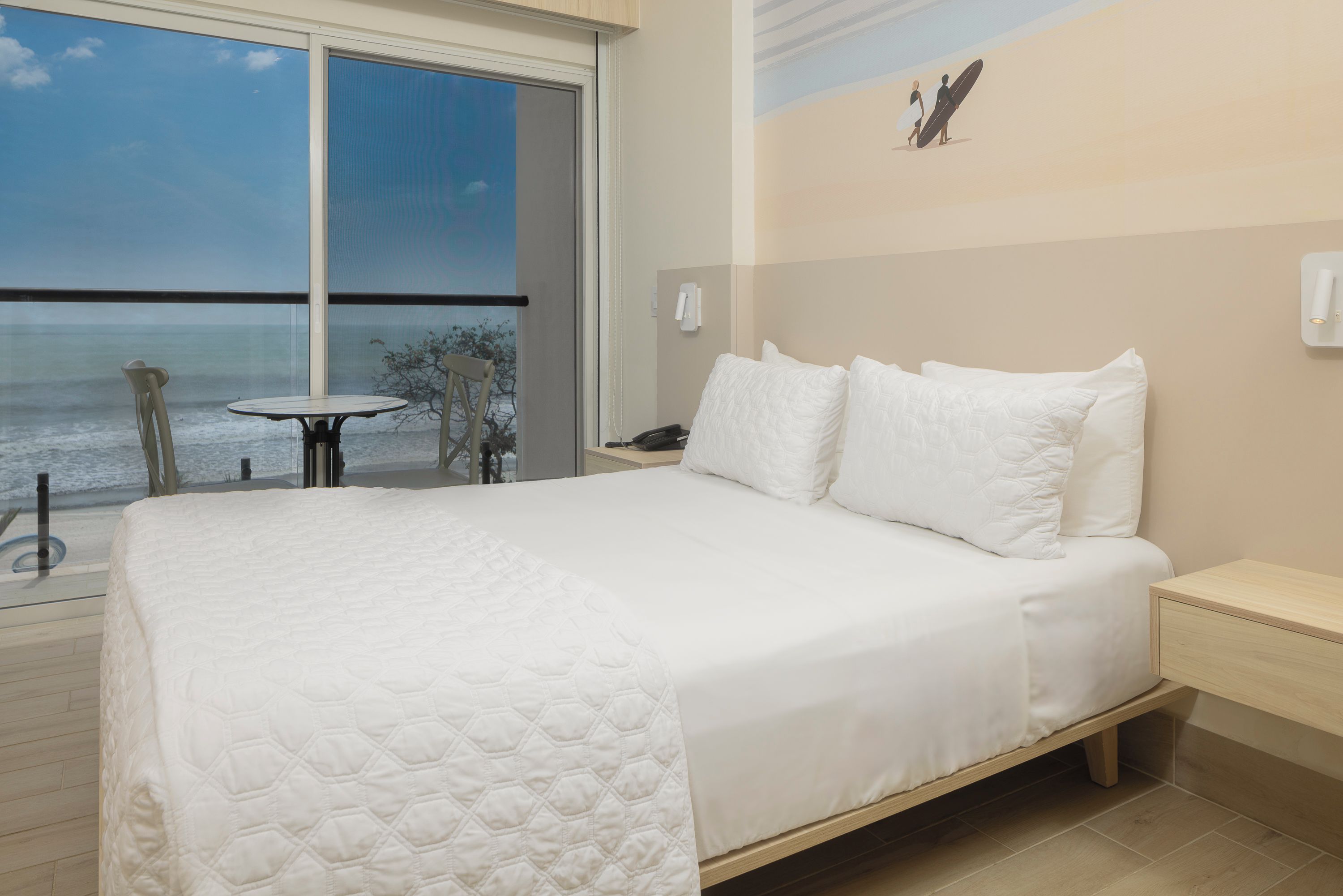A hotel room with a large bed, a small table, and a view of the ocean.