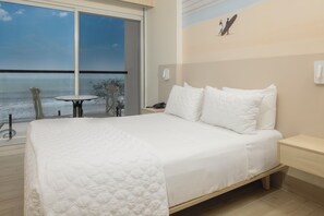 A hotel room with a large bed, a small table, and a view of the ocean. - Radisson Riviera Panama (Las Huacas)