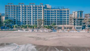 A beachfront hotel with multiple floors, a sandy beach in the foreground, and a clear blue sky.