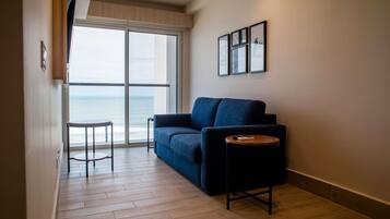 Un salon moderne avec un canapé, une petite table ronde et une vue sur la mer, visible à travers une grande fenêtre.