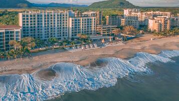 A coastal hotel with multiple high-rise buildings, a sandy beach, and waves approaching the shore.