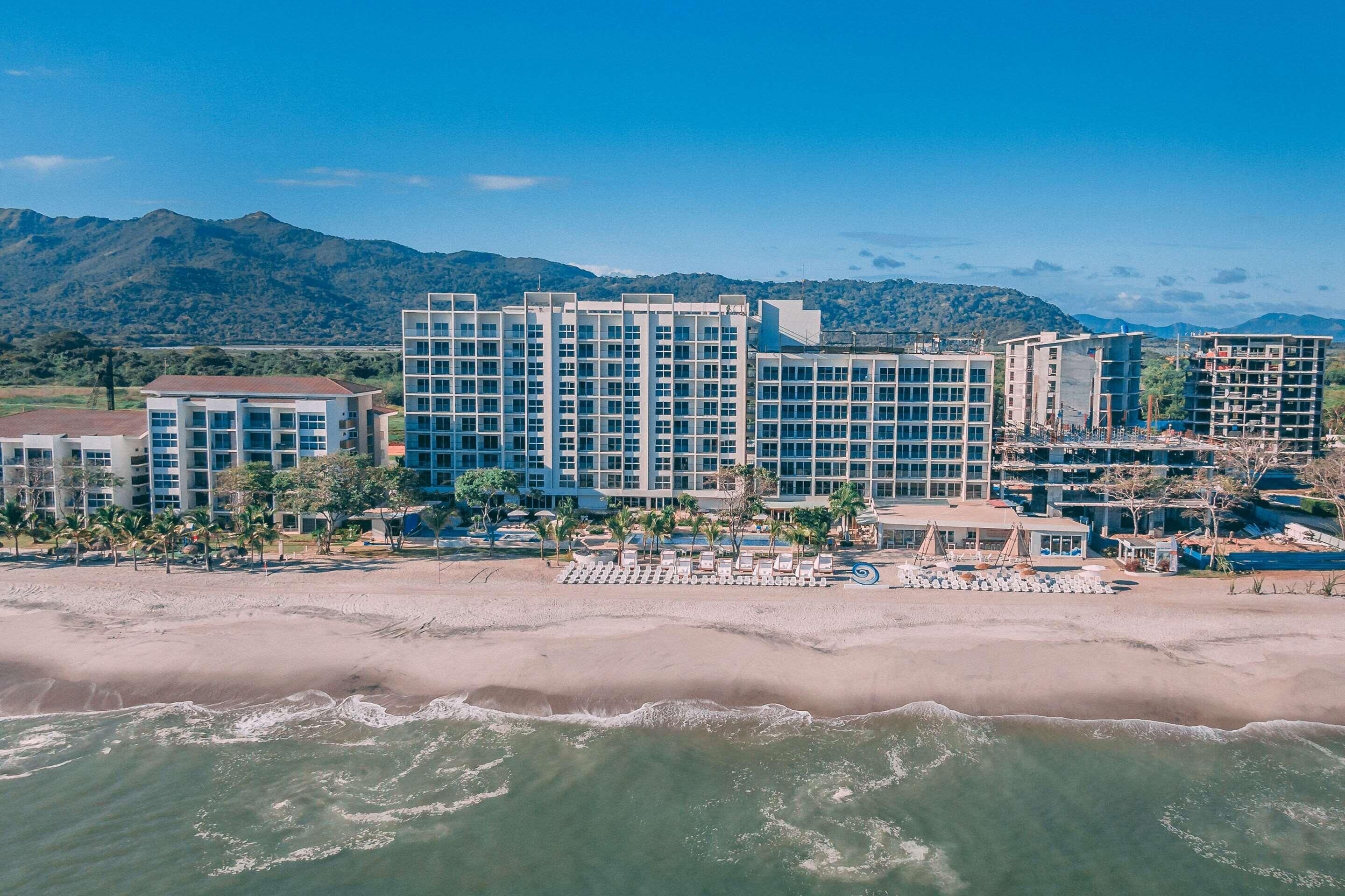 A beachfront hotel with multiple buildings, a sandy beach, and ocean waves.