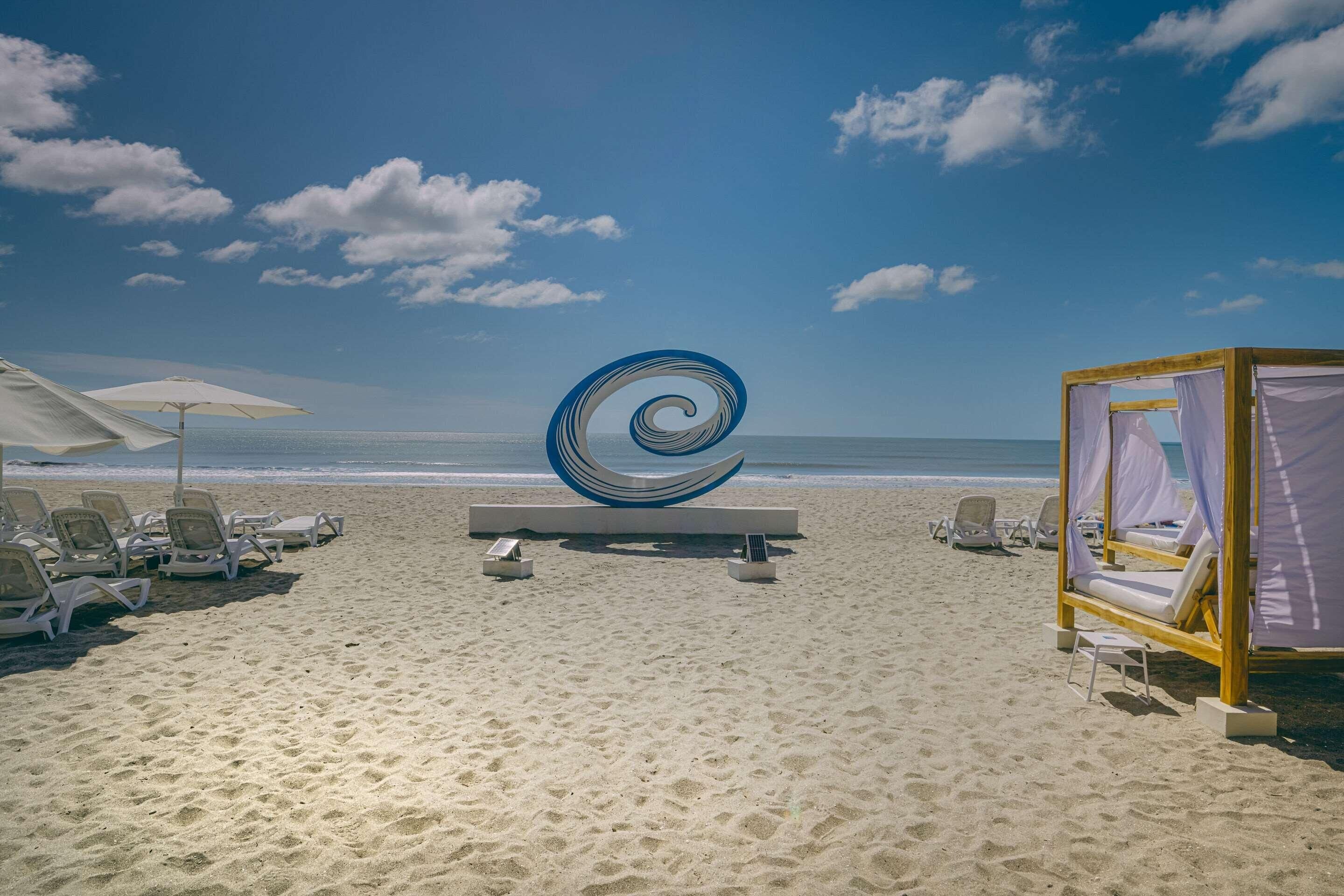 Una playa con sillas de descanso, una gran escultura en espiral y una cabaña de madera.