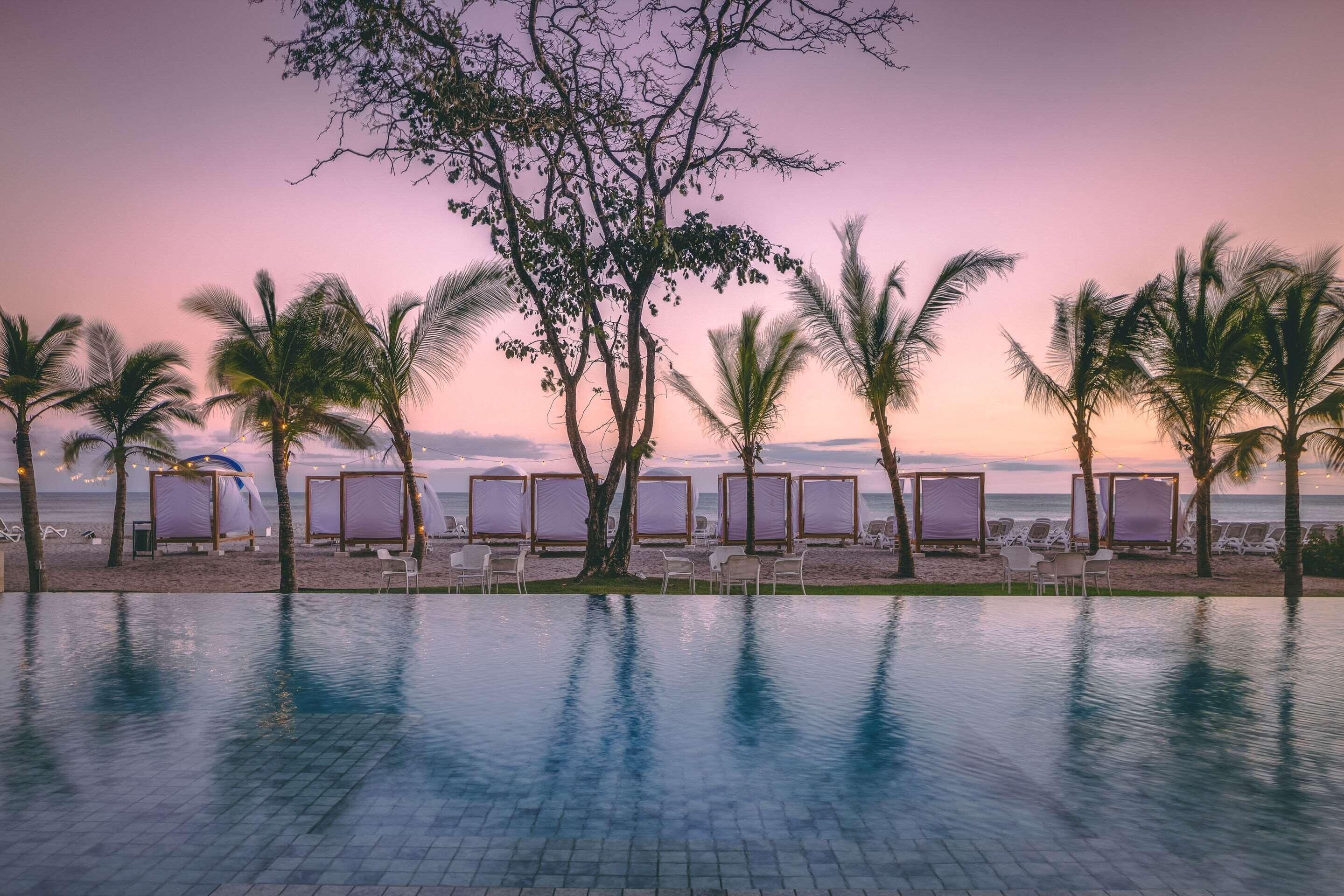 Un espace aménagé au bord de la piscine, avec des chaises longues et des parasols, offrant une vue sur la plage et l’océan.