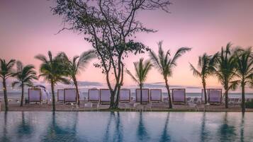 Un espace aménagé au bord de la piscine, avec des chaises longues et des parasols, offrant une vue sur la plage et l’océan.
