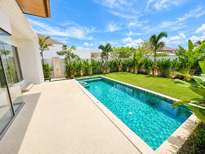 A modern pool area with a clear blue pool, surrounded by lush greenery and a well-maintained lawn. - Brand New Private 3-bedroom Pool Villa in Bang Tao, Phuket (Thep Krasattri)