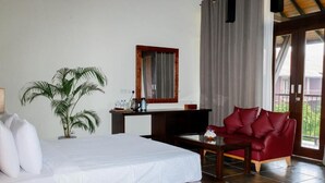 A bedroom with a bed, a red sofa, a coffee table, a TV, a potted plant, and a window with curtains. - Celestia Ayurveda Resort (Bentota)