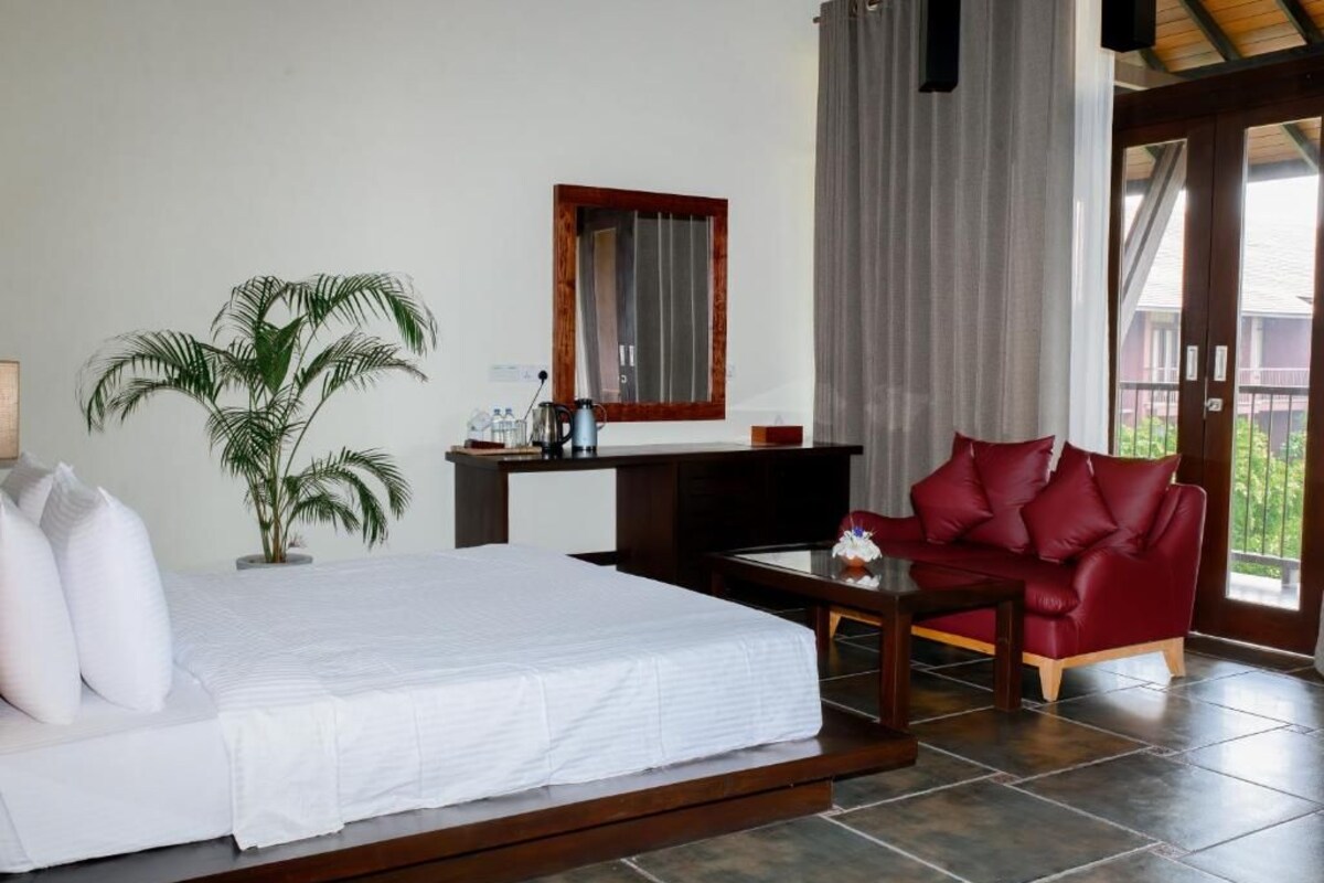 A bedroom with a bed, a red sofa, a coffee table, a TV, a potted plant, and a window with curtains.