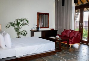 A bedroom with a bed, a red sofa, a coffee table, a TV, a potted plant, and a window with curtains. - Celestia Ayurveda Resort (Bentota)