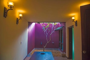 A hallway with a tree, purple walls, and wall-mounted lights.