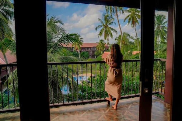 A person on a balcony with a view of a pool and palm trees.