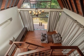 A spacious room with a wooden staircase, a chandelier, and a view through large windows.