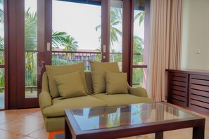 A room with a sofa, a glass coffee table, and a view of palm trees through large windows.