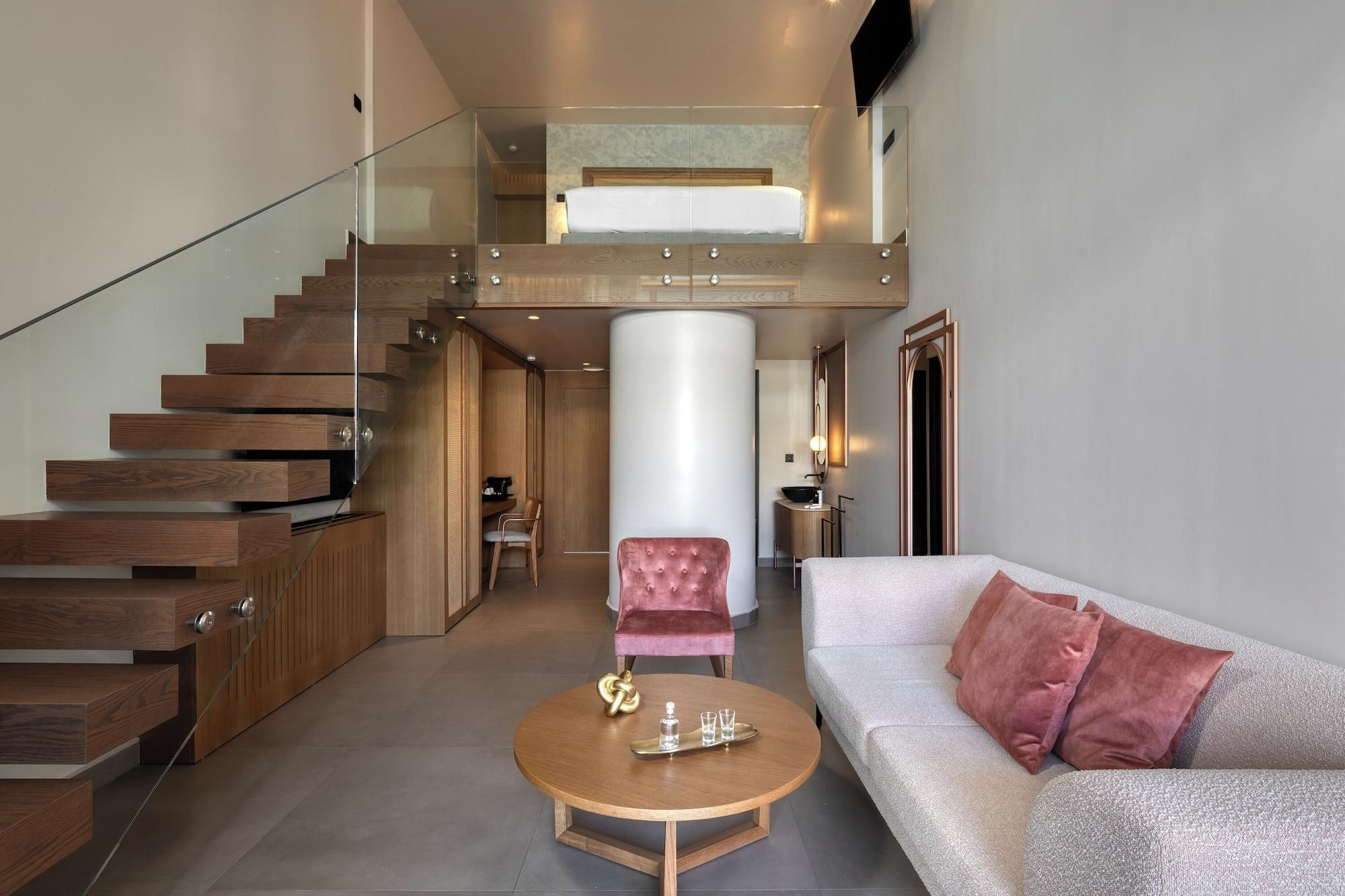 A modern interior with a staircase, a round wooden coffee table, a cushioned sofa, and a pink chair.