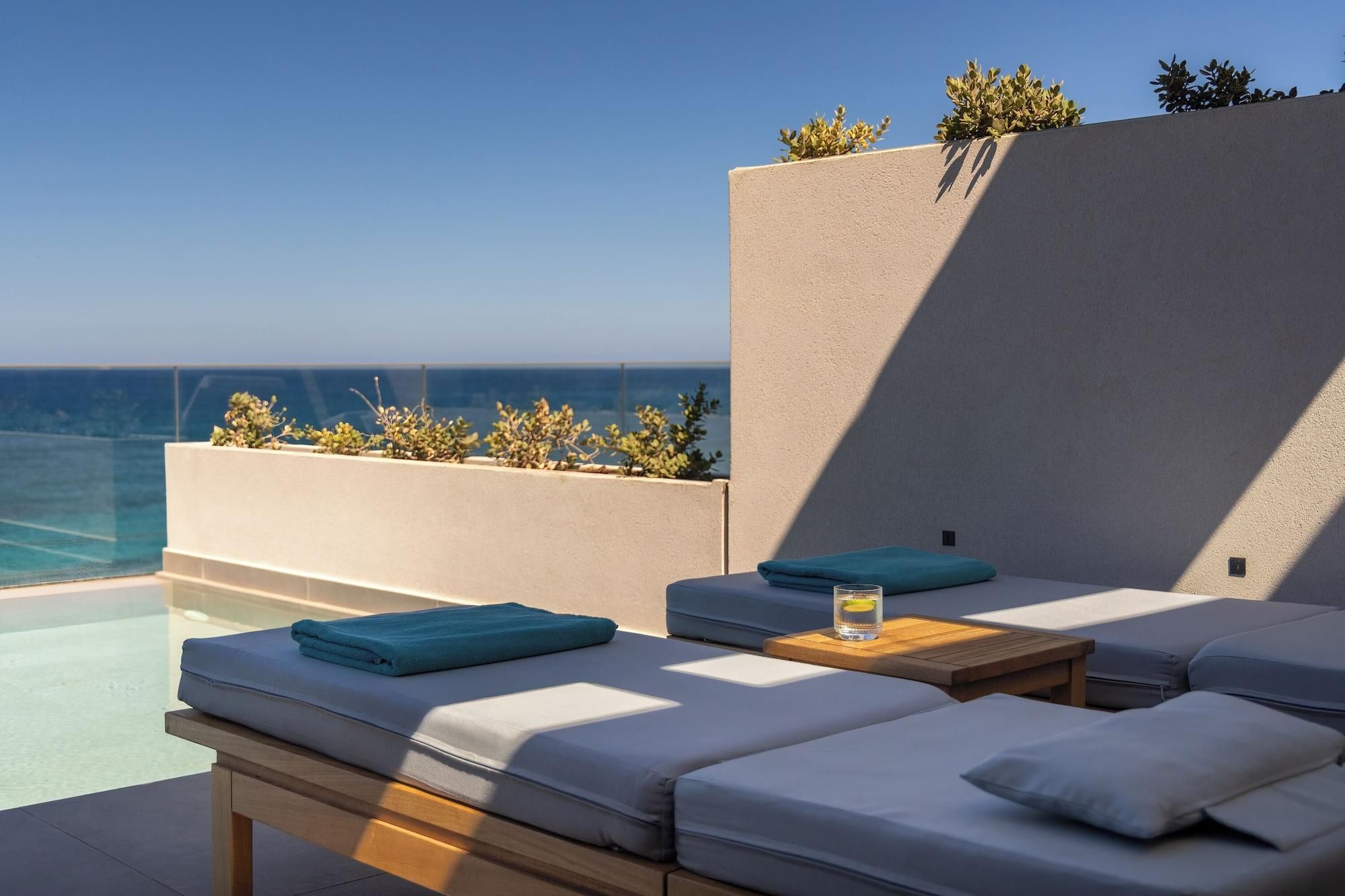 A sunlit outdoor seating area with a pool, cushions, and a wooden table.