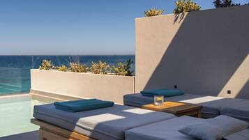 A sunlit outdoor seating area with a pool, cushions, and a wooden table.