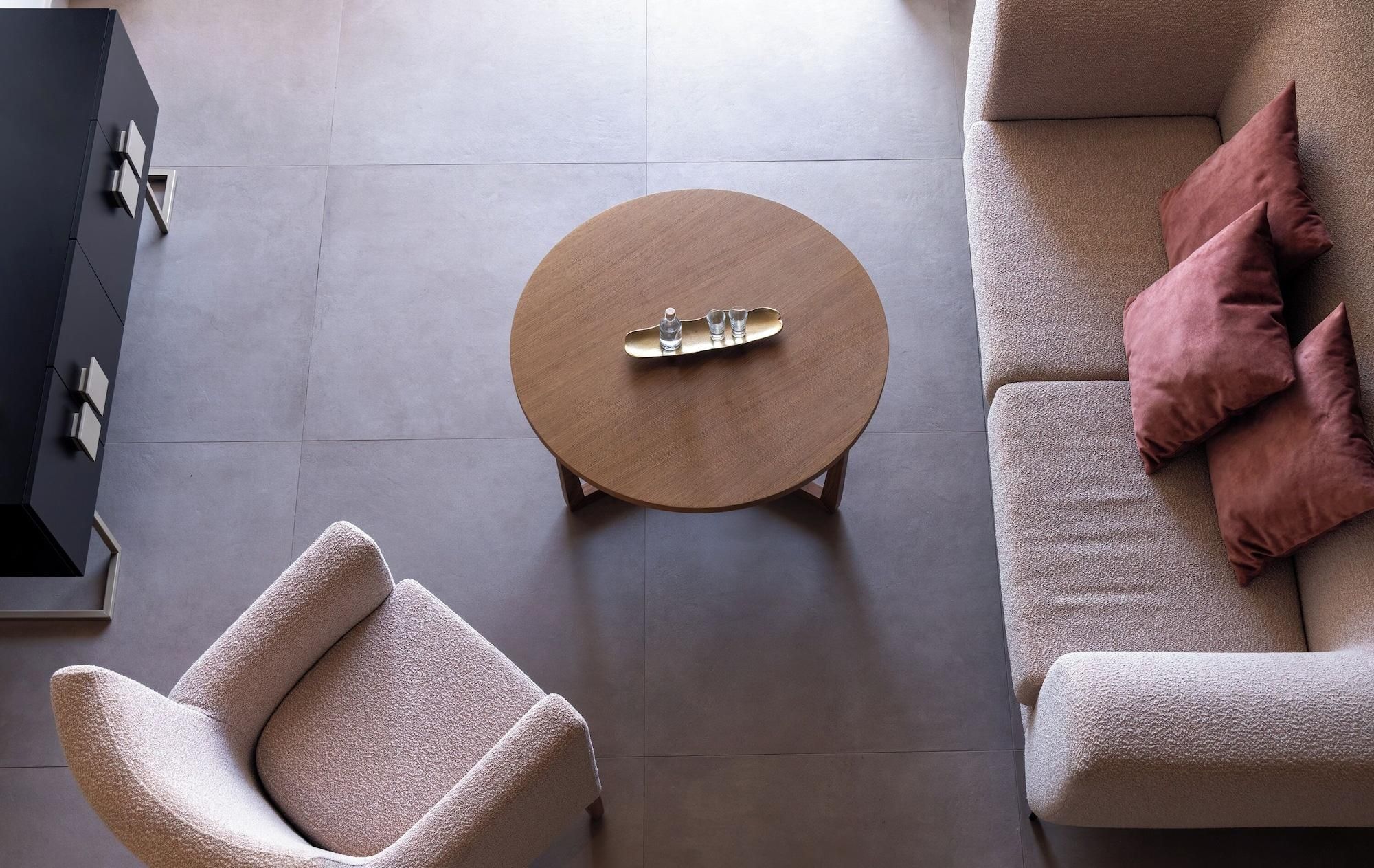 Una sala de estar moderna con una mesa de centro redonda de madera, un sillón color beige y un sofá con cojines rosados.
