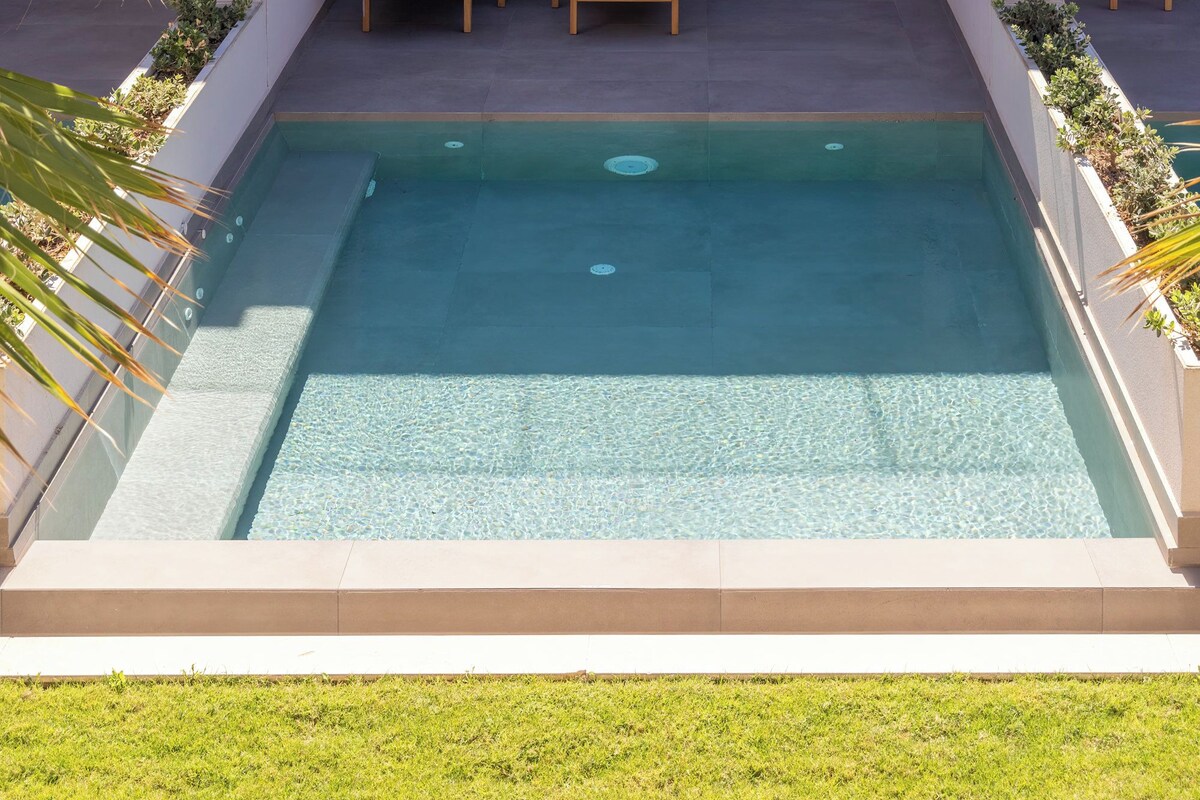 Un área de piscina moderna al aire libre con sillones de descanso y un porche con paredes de vidrio.
