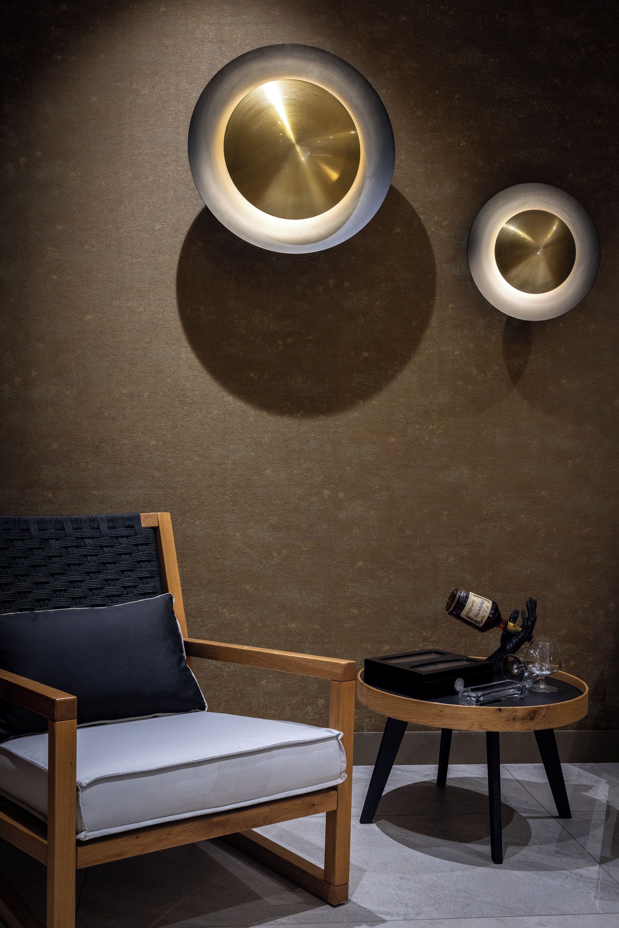 A modern room with a wooden chair, a small round table with a bottle and glass, and two wall-mounted circular light fixtures.