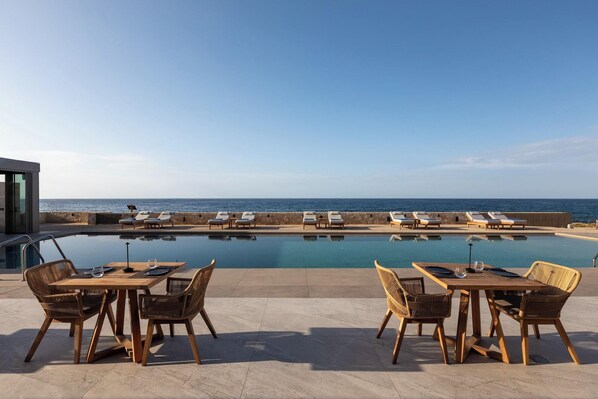 A poolside area with lounge chairs and tables, overlooking a body of water. - Castello Boutique Suites By The Sea (Agios Nikolaos)