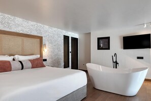 A modern bedroom with a large bed, a freestanding bathtub, and a television mounted on the wall. - Castello Boutique Suites By The Sea (Agios Nikolaos)