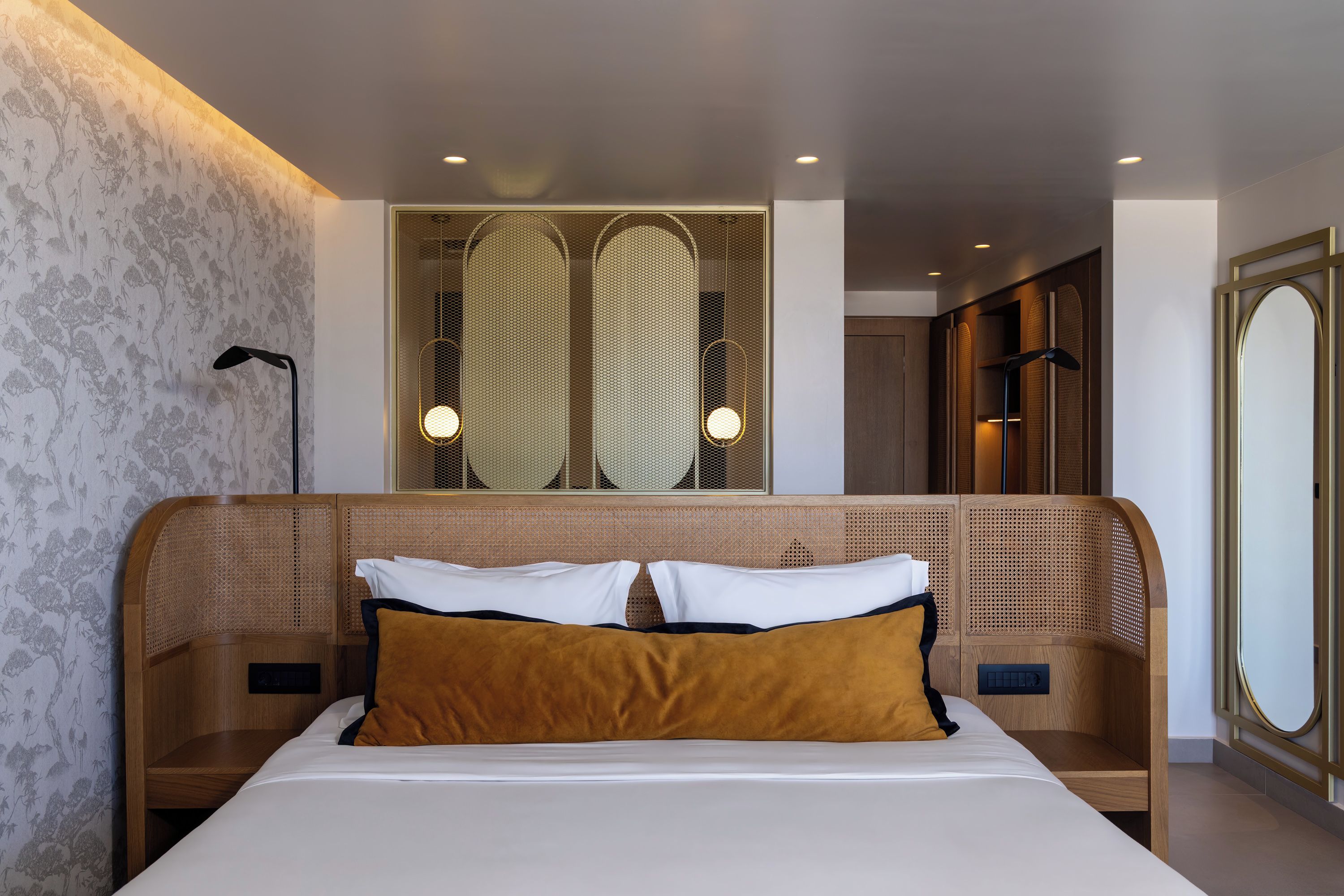 Habitación de hotel moderna con una cama grande, cabecera de madera, un espejo amplio y un panel decorativo en la pared.
