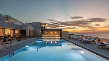Zona de piscina con sillones de descanso y un bar, con vista a una extensión de agua al atardecer.