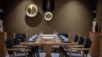 A dining area with a long wooden table set for a meal, surrounded by chairs with cushioned seats.