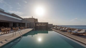 Ein Poolbereich mit Liegestühlen und einer Bar mit Blick aufs Meer.