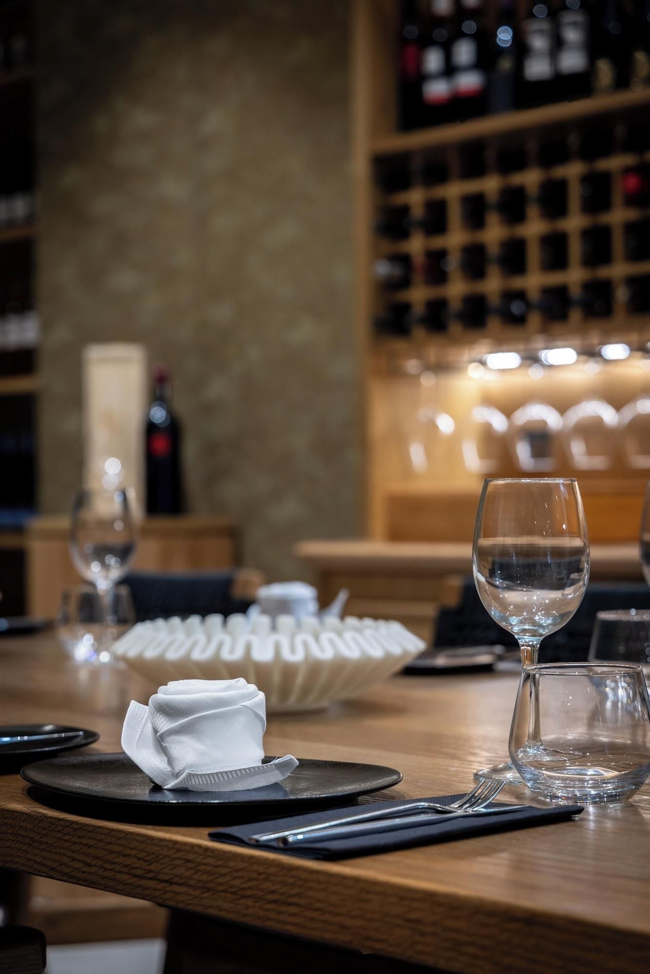 Un bar con una botella de vino, un vaso de agua, y platos y cubiertos ordenados.