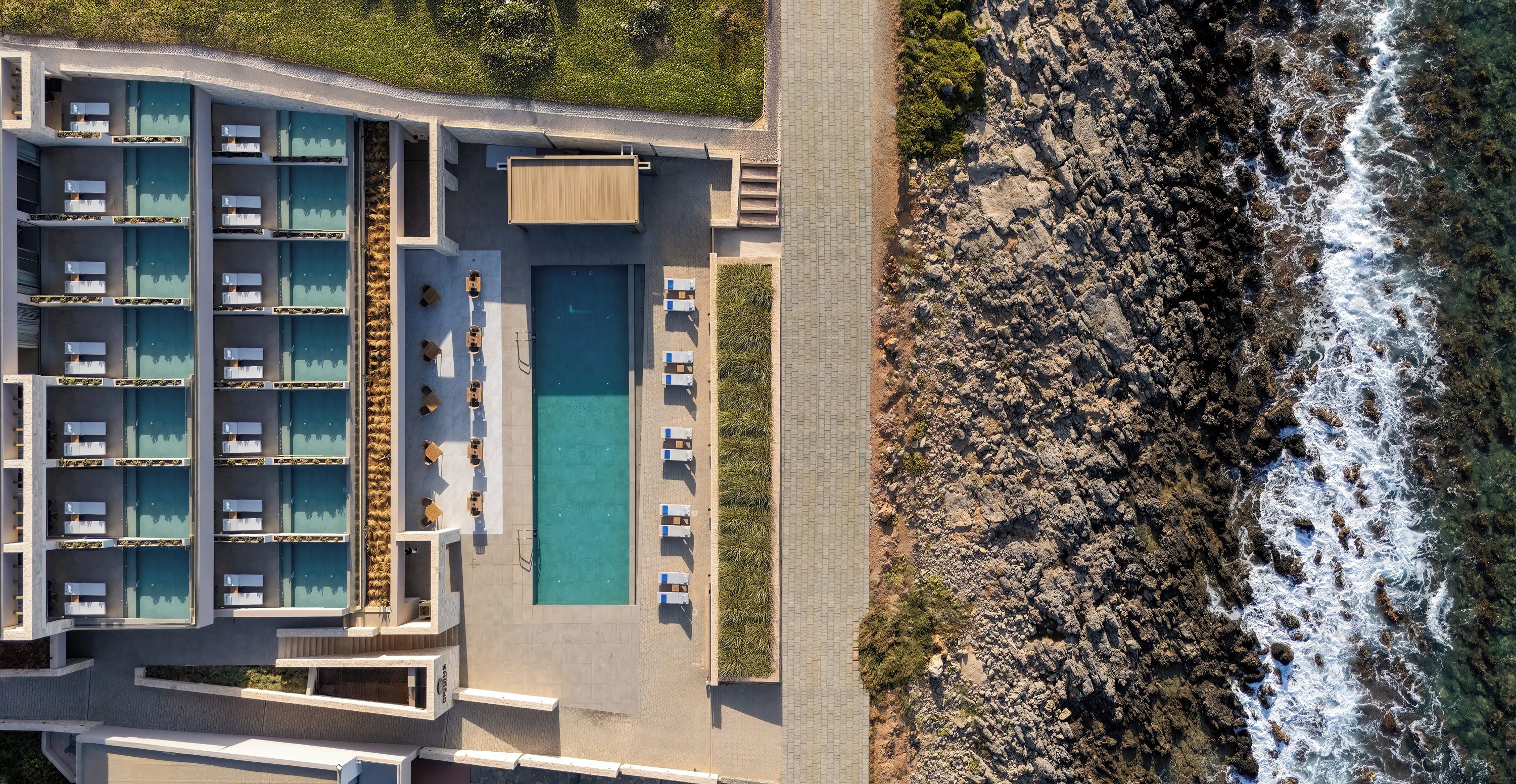 An aerial view of a hotel with multiple swimming pools, a beachside location, and rocky coastline.