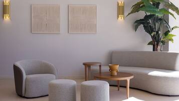 A modern living room with a grey sofa, two armchairs, a coffee table, and a large plant.
