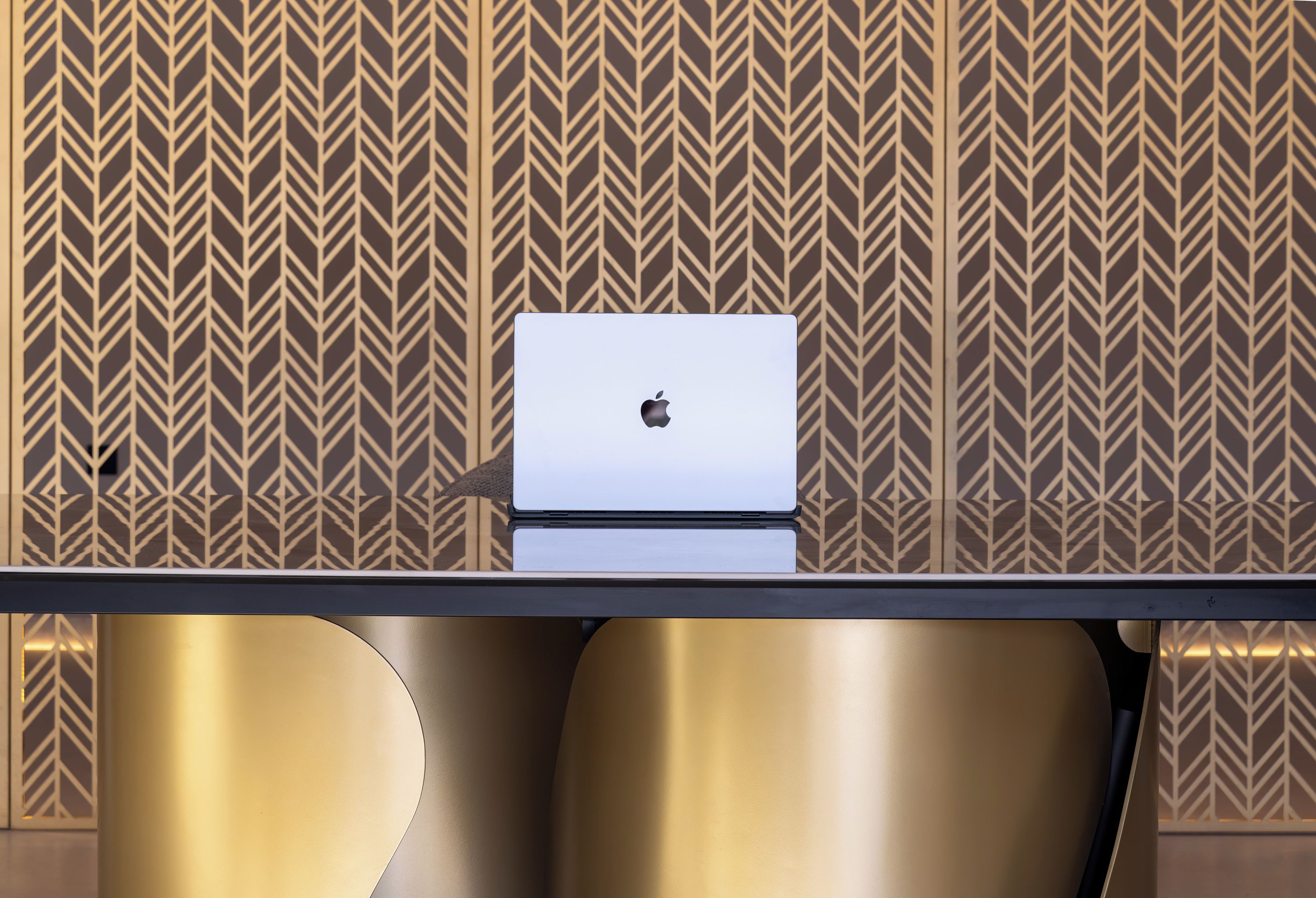 A modern room with a sleek table, a laptop, and a patterned wall.