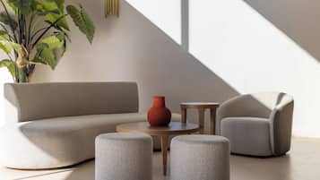 Ein modernes Wohnzimmer mit einer Couch, zwei Hocker, einem kleinen Tisch und einer Topfpflanze.