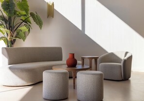 A modern living room with a sofa, two ottomans, a small table, and a potted plant. - Castello Boutique Suites By The Sea (Agios Nikolaos)