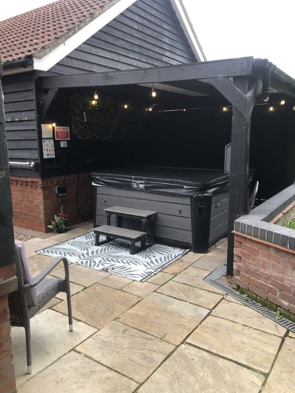 Ein überdachter Grillbereich im Freien mit Grill, Sitzgelegenheiten und Lichterketten.