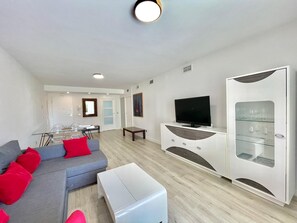 Een moderne woonkamer met een grijze bank, een flatscreen-televisie en een kast met glazen deuren en wijnglazen.