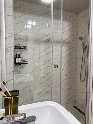 A bathroom with a glass-enclosed shower, marble walls, and a white bathtub. - Zarafshan 60 (Tashkent)
