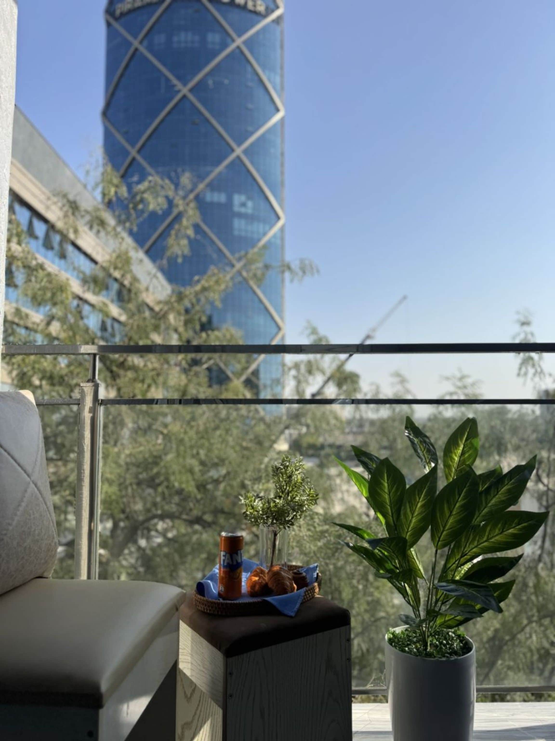 Un balcón con vistas a un edificio moderno, una pequeña mesa con una planta y un refrigerio, y un sofá.