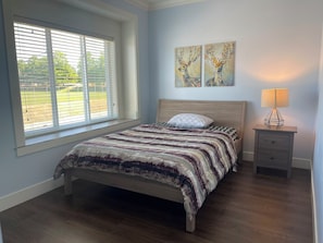 A bedroom with a bed, a window, a nightstand with a lamp, and two wall-mounted paintings. - Beautiful Master room house in Coquitlam perfect for your next stay- (Coquitlam)