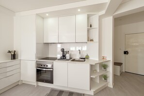 A modern kitchen with white cabinetry, a built-in oven, a coffee machine, and a sink. - Caparica Sunny Apartment by Homing (Almada)