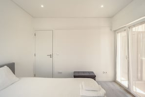 A bedroom with a bed, a bench, a door, and a window. - Caparica Sunny Apartment by Homing (Almada)