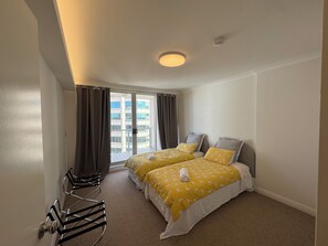 Ein Hotelzimmer mit zwei Betten, einem Sessel, einem Fenster mit Vorhängen und einer Deckenleuchte.