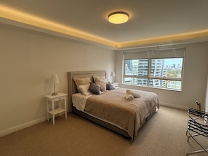 A bedroom with a bed, nightstands, a window with a city view, and a ceiling light. -  2 Bdrm Apart -90m2, 2mins walk station Free Carpark (Chatswood)