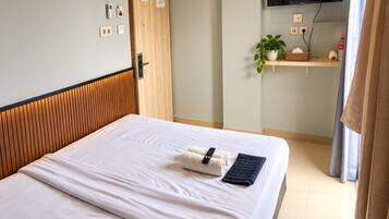 A hotel room with a bed, a television mounted on the wall, a small shelf with a plant, and a door with a wooden panel.