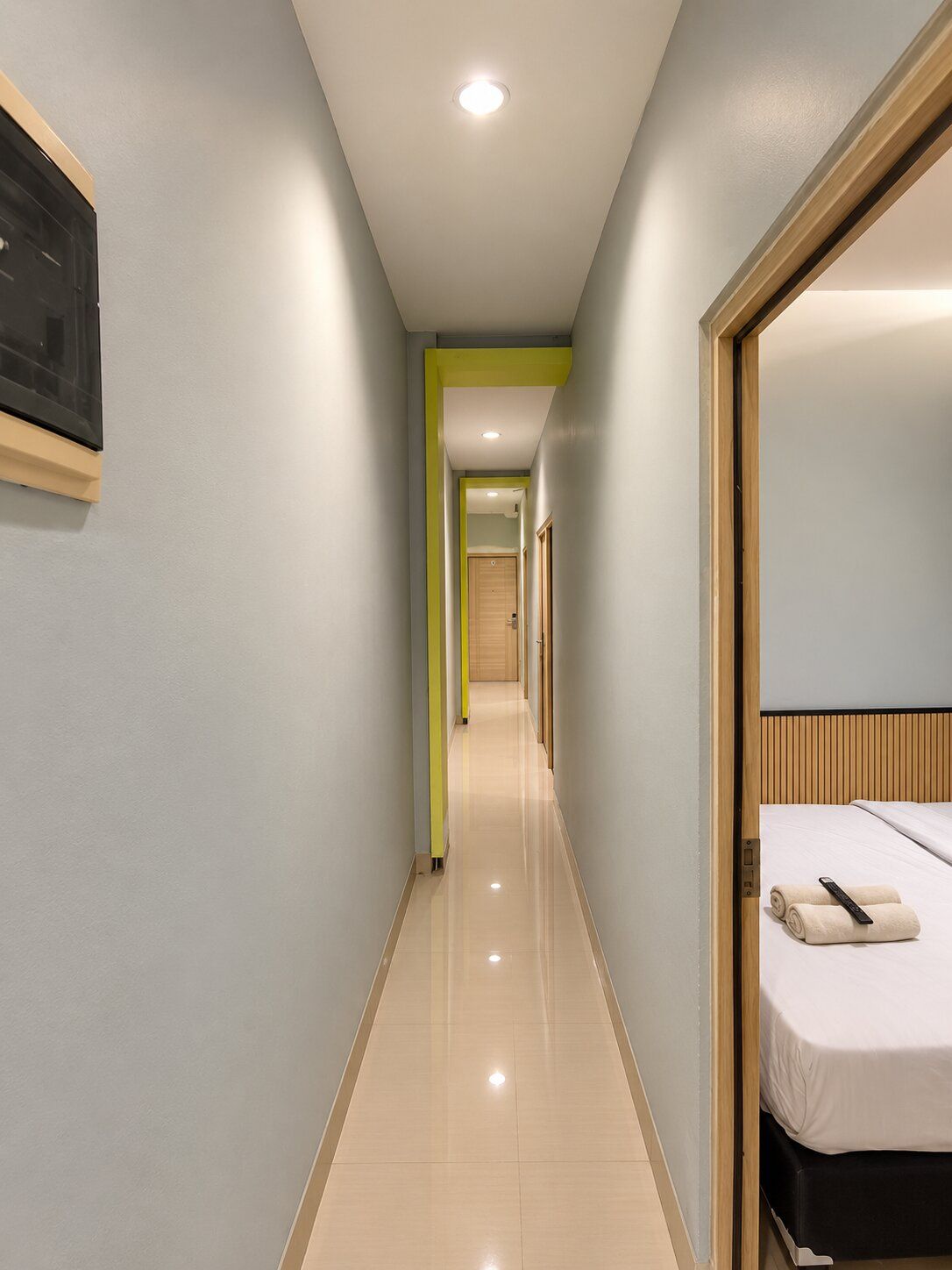 A hotel corridor with a bed on the right, a door at the end, and a light-colored floor.